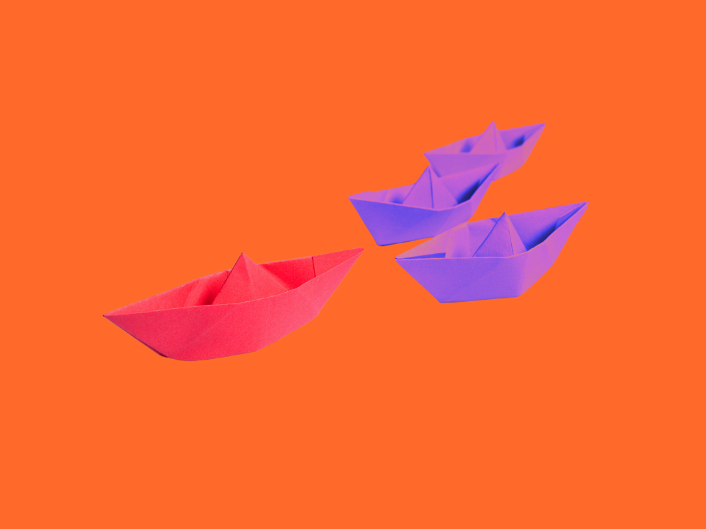 A red paper boat in front of three purple paper boats.