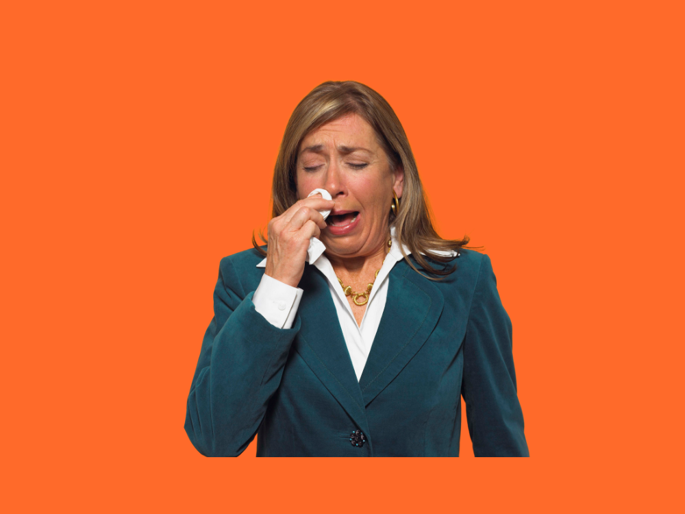 A woman wearing a green jacket is crying and wiping her eyes with a white tissue